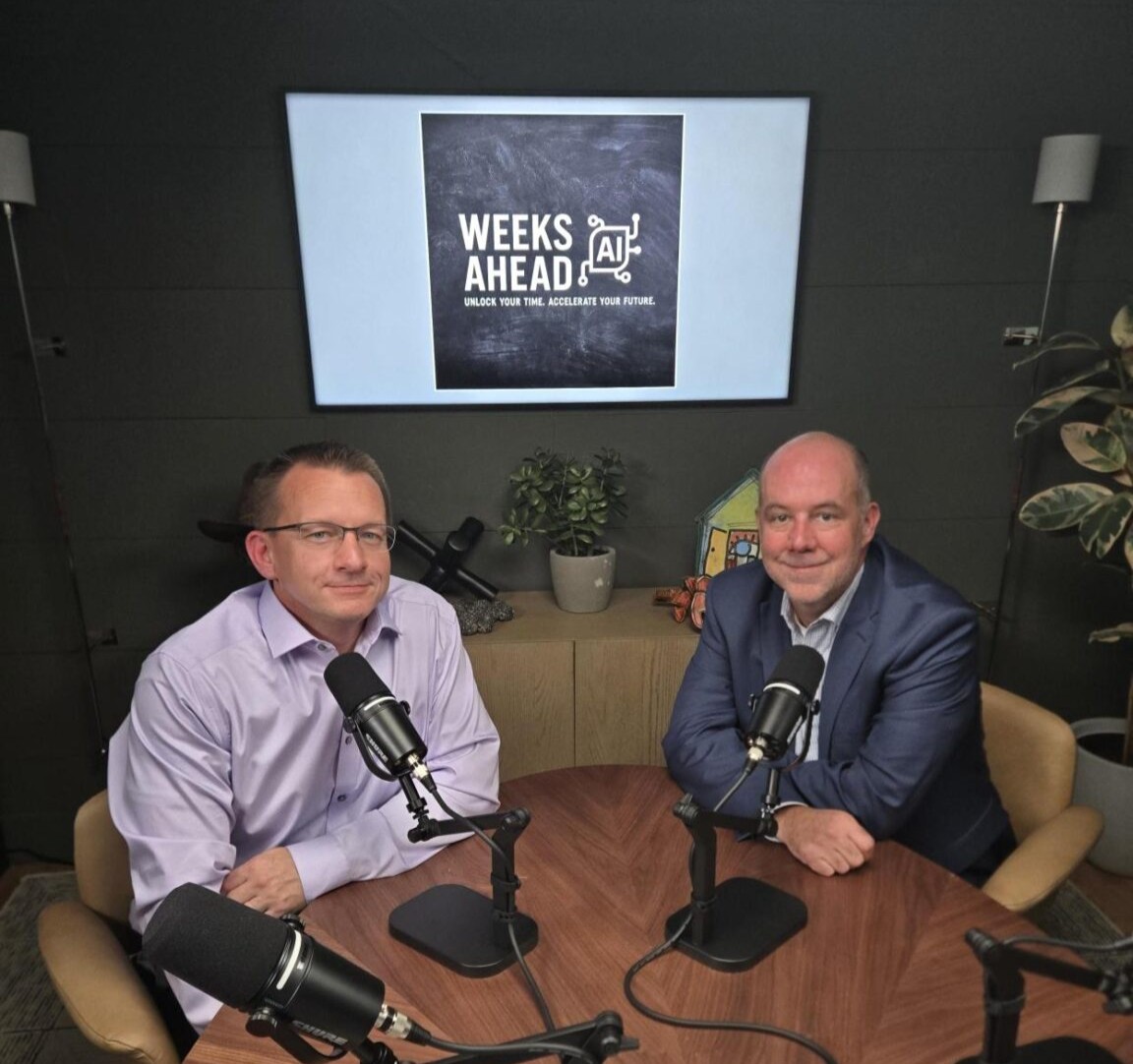 Two men sit at a round wood table with black podcast microphones, in front of a wall screen that reads Weeks Ahead.