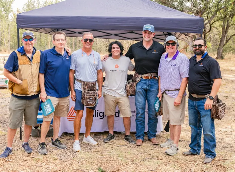 Aligned Technology Partners team members and their families standing together under a canopy at the Christ’s Haven Clay Shoot at Northlake Shooting Sports.